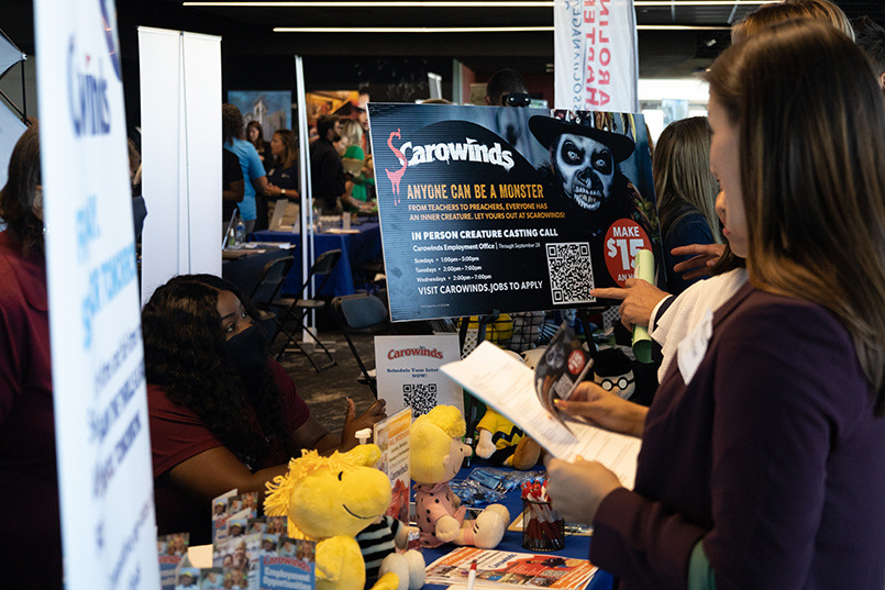 Charlotte, North Carolina, amusement park Carowinds has its sign for the annual Scarowinds event in the background of its table while a recruiter for them talks with students at the Experience Expo job fair.