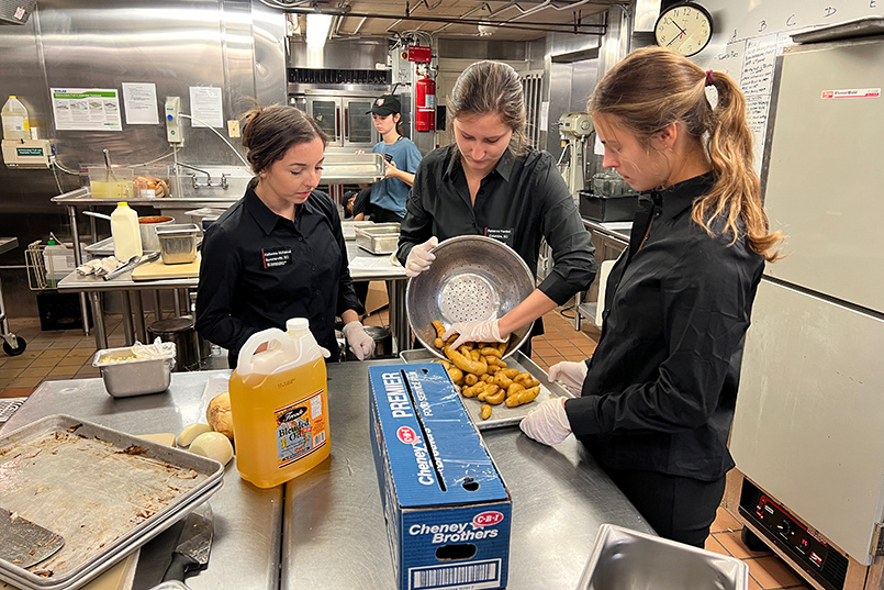 Three students pour cooked potatoes onto a baking sheet in the McCutchen House kitchen.