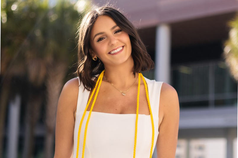 Georgia Filter poses for a photo wearing her yellow graduation cords around her neck.