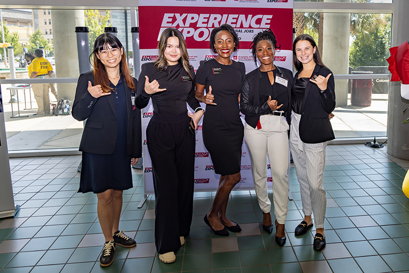 Five members making up the College of HRSM's corporate engagement team pose for a photo while throwing up the Spurs Up sign at Experience Expo.