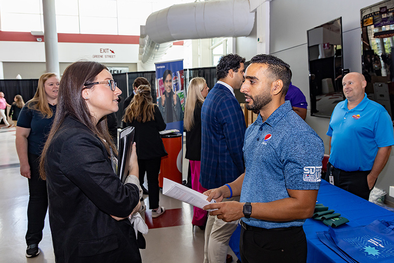 A member of PepsiCo holds a document while speaking to an HRSM student at Experience Expo.