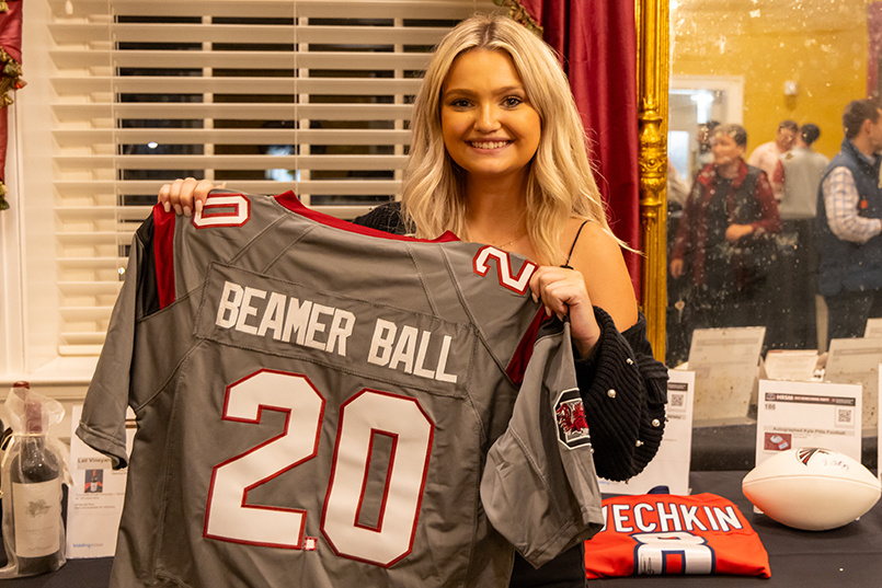 A person holds up a football jersey with the name Beamer Ball on the back and the number 20.
