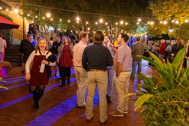 A crowd of people talk amongst themselves outside of McCutchen House near the dance floor area for the 2023 Homecoming Party.