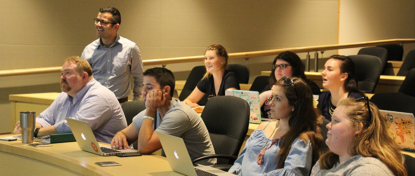 Armen Shaomian stands near his students in the classroom while viewing an entertaining video on the widescreen.