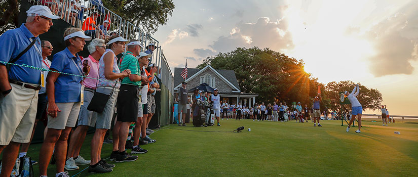 Country Club of Charleston plays host to the 2019 U.S. Women's Open Golf Tournament. In this photo of the club event, a golfer tees off while a large group of fans looks on.