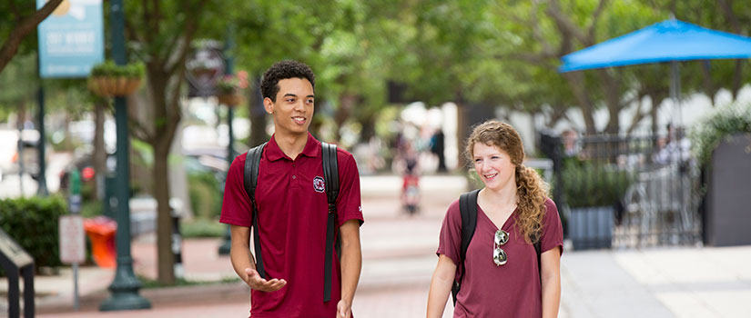 Two HRSM students walk on Main Street amidst green trees, hanging flowers and cafes in beautiful downtown Columbia.