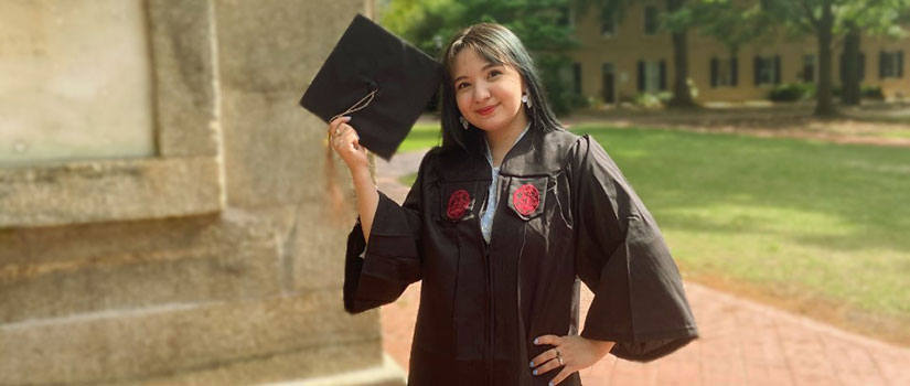 Ashley Ooi holds her graduation cap above her head as she stands beside the Maxcy Monument on the historic UofSC Horseshoe.