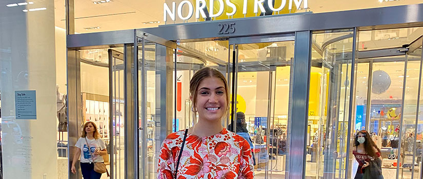 Kate Valaoras stands smiling in a colorful dress in front of the Nordstrom store in NYC.