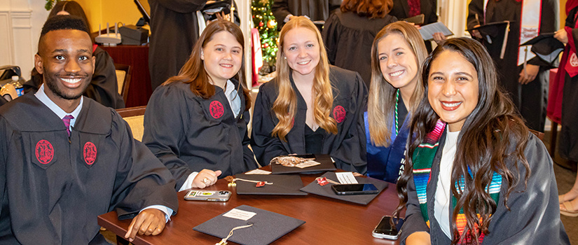 Five HRSM graduates pose for a photo around a table at McCutchen House.