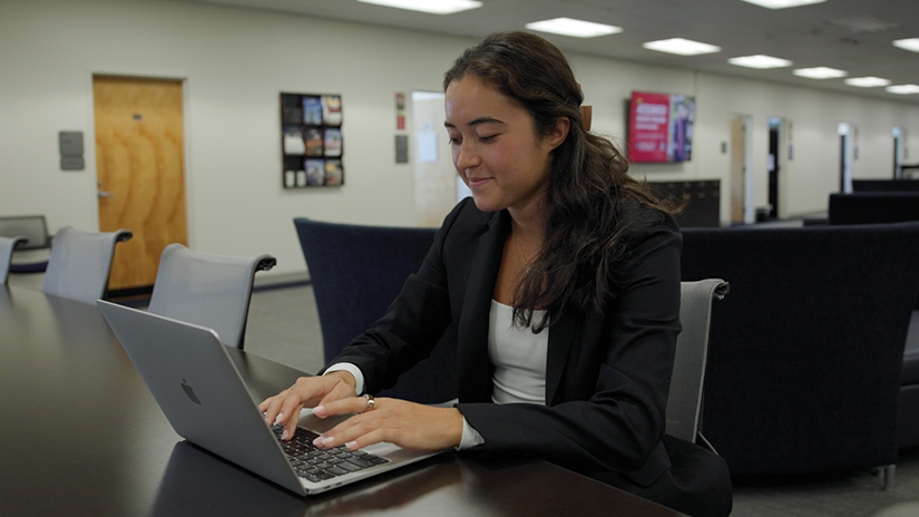 Josie Anaya, a hospitality management student at the University of South Carolina, works on her laptop in a study lounge while wearing a black blazer and white top.