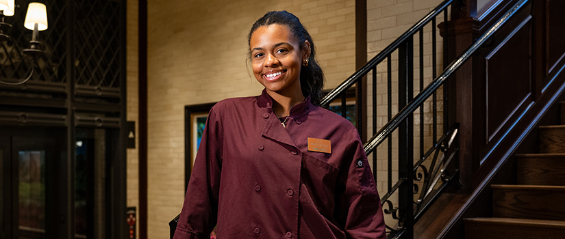 USC student in a maroon Masters uniform standing by a staircase and smiling during her tournament experience.