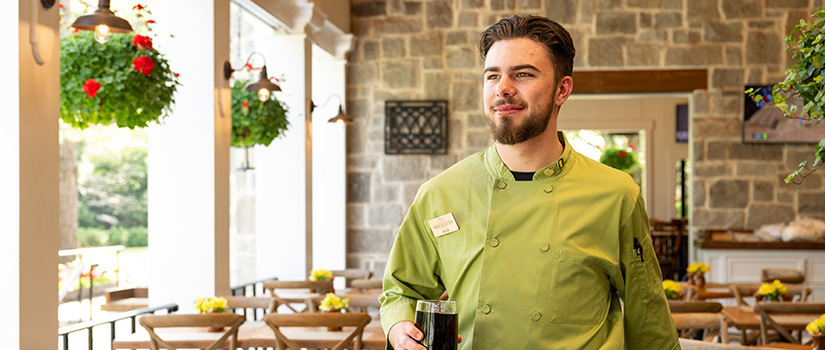 USC student in a green Masters uniform holding a drink while working at Augusta National Golf Club.