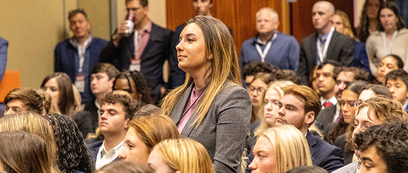 A large audience of USC sport and entertainment management students sits attentively during a SEVT Conference session, with one student standing to ask a question while faculty, recruiters, and industry professionals look on from the back of the room.