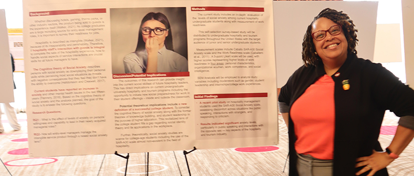 Katheldra Alexander stands beside her research poster on student social anxiety and emerging hospitality leaders at an academic research conference.
