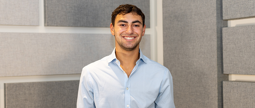 Trevor Lazarus smiles in a portrait wearing a light blue button-down shirt in front of a wall of gray acoustic panels.