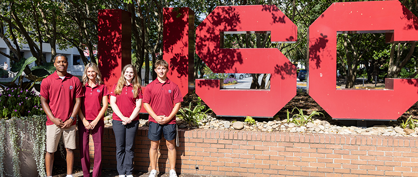 Four members of the seventh cohort of Tepper Scholars stand together in front of the large USC letters on the University of South Carolina campus.