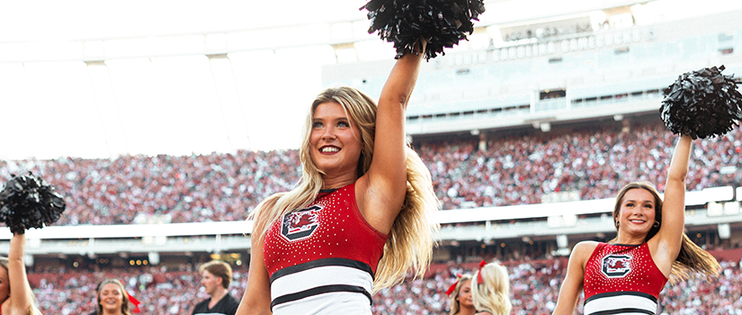The University of South Carolina Carolina Dance Team poses for a group photo on the field at Williams-Brice Stadium, wearing garnet and white uniforms.