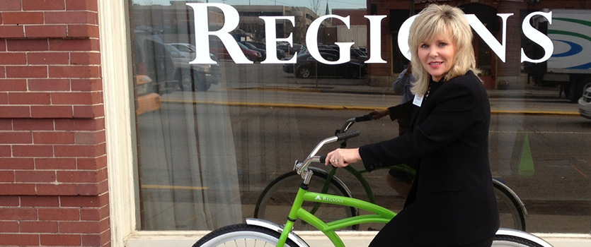 Cathy Jansen rides her green Regions bike in front of the Regions Bank.