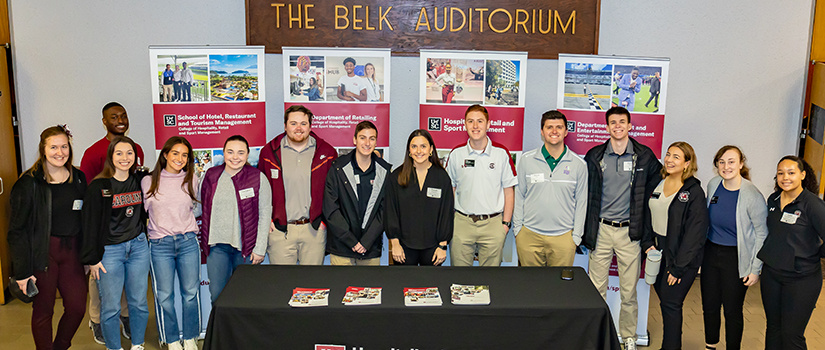 Fourteen College of HRSM students pose for a photo outside the Belk Auditorium.