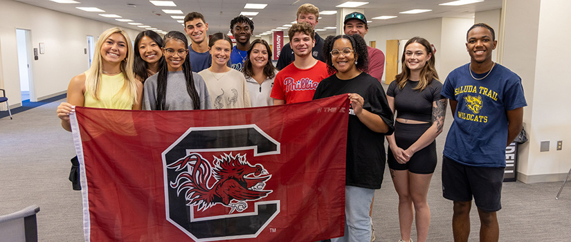 A group of HRSM students pose with a Block C Gamecock flag on the sixth floor of the Close-Hipp Building