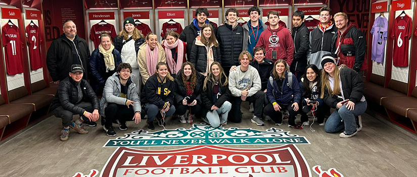 Students and HRSM faculty/staff pose for a photo inside the locker room of Liverpool football club in England during a spring break study abroad trip.
