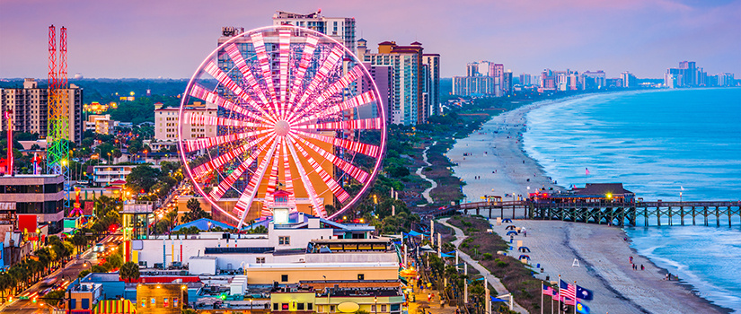 An overhead shot of the Grand Strand in Myrtle Beach, South Carolina, with a large Ferris wheel prominently featured at dusk.