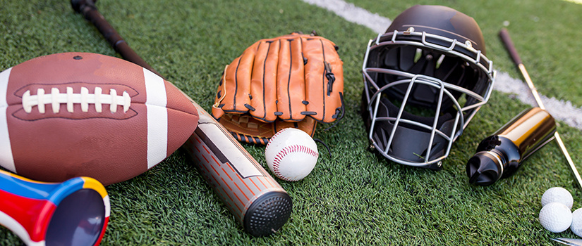 A collection of sports equipment including a baseball bat, baseball, football, football helmet, golf club and golf balls.
