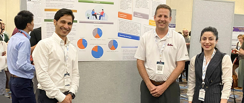 Two sport and entertainment management Ph.D. students pose for a photo with professor Stephen Shapiro at a conference.