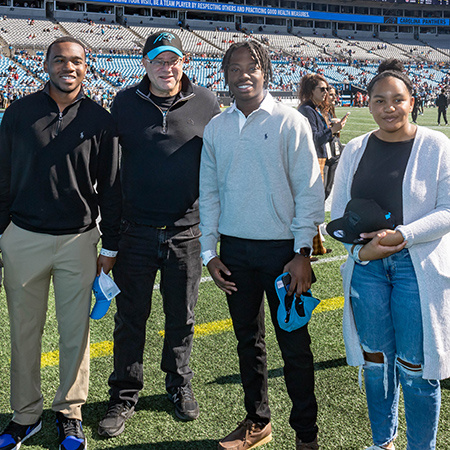 Tepper Scholars Todd Hardy, Jeremiah Smith and Sydney Rhue pose for a photo with David Tepper on the field at Bank of America Stadium prior to a Panthers game.