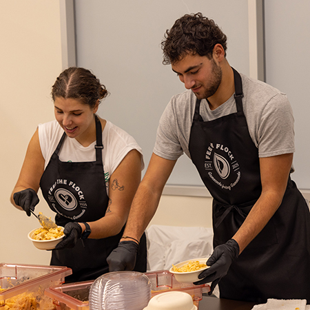 Two USC students wearing Feed the Flock aprons portion food into compostable bowls inside the Marriott Culinary Lab kitchen.