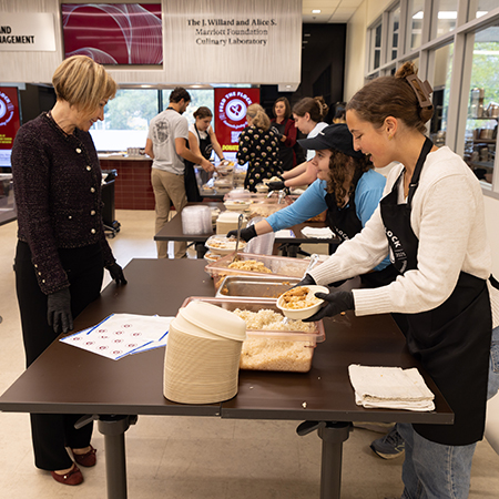 USC First Lady Ero Aggelopoulou-Amiridis talks with students preparing meals during a Feed the Flock volunteer event in the Marriott Culinary Lab.