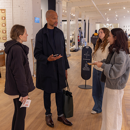 USC retailing students gather around Instructor Donald Pollard as he discusses retail career insights inside a modern High Point Market showroom with art and furnishings on display.