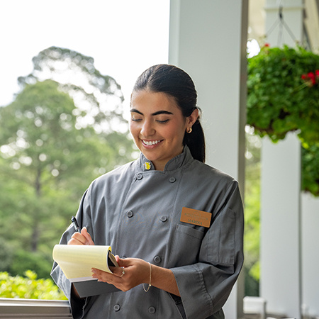 USC student in a gray uniform smiling and taking notes while working at the Masters Tournament.