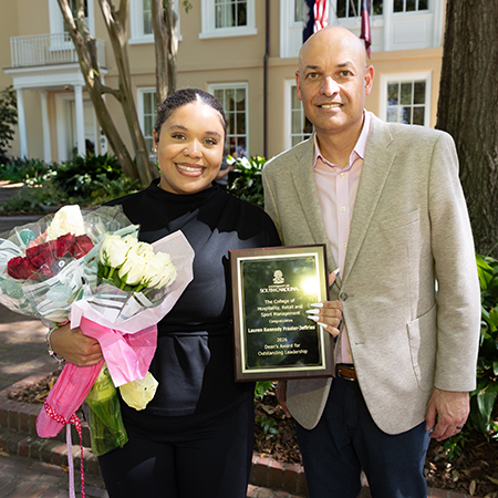 Lauren Frasier-Jeffries stands outdoors with flowers and her HRSM Dean’s Award for Outstanding Leadership beside Dean Michael Sagas at USC Awards Day.