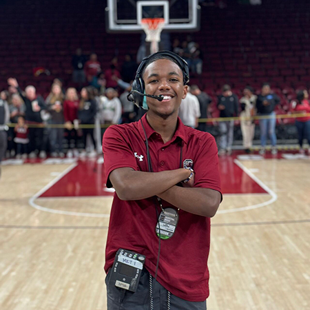 Branden Miller working courtside during a South Carolina Gamecocks women’s basketball game wearing a headset and event credentials.