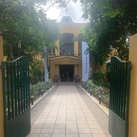 Gates are open leading to the entrance of a building at the University of Aruba.