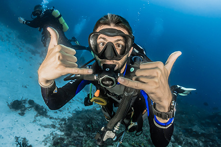 A diver underwater flashes the Spurs Up sign for the camera. Another diver is visible in the background.