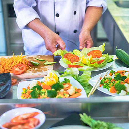 A chef stands over a colorful display of salads.