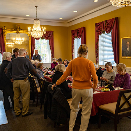 A large group of customers sit and stand around a dining table at the McCutchen House.
