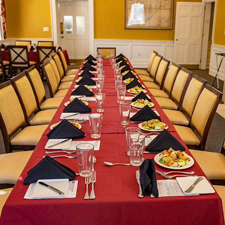 A large table has been prepped with salads at each seat along with silverware, drinks, plates and napkins.