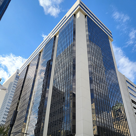 Exterior view of a modern high-rise office building with reflective glass windows and white architectural columns, photographed from street level against a blue sky with scattered clouds.