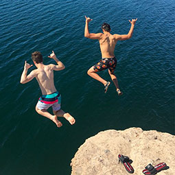 Spencer Swearingen and a friend (caught mid-air) give the "spurs up" hand sign while jumping off a rock into a lake. Spencer's gamecock shower shoes are left sitting on the rock.