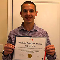 Michael Sisk stands holding his accreditation certificate. Michael became an NCAA accredited personal trainer through the American Council on Exercise. 