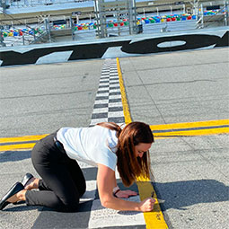 Julia McAleer kneels on the Daytona Raceway and signs her name on the pavement of that legendary racetrack