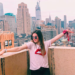 Sara Polllin, with arms spread wide, stands on a patio overlooking New York City buildings