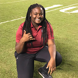Lyric Swinton kneels on a football field and gives the "spurs up" hand signal