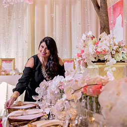 Nirjary Desai stands in a room decorated for a bridal reception with lush flowers and formal table setting