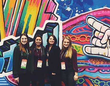 Students pose in front of a colorful mural while visiting San Francisco for the Professional Convention Management Association Convening Leaders Conference.