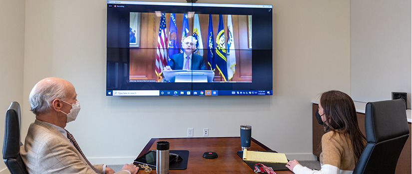 Dean Hubbard and Associate Professor Lisa Martin watch the TV monitor as Attorney General Merrick Garland speaks during an event recognizing law schools for their efforts to fight the housing and eviction crisis.