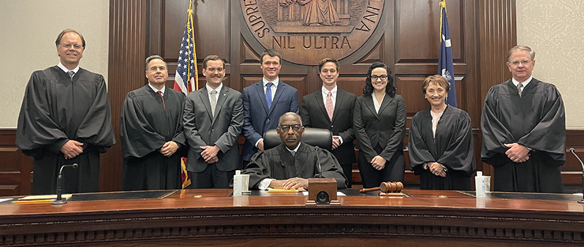 members of the Moot Court team surrounded by members of the South Carolina Supreme Court and standing behind the Supreme Court bench with the Supreme Court seal in the background.